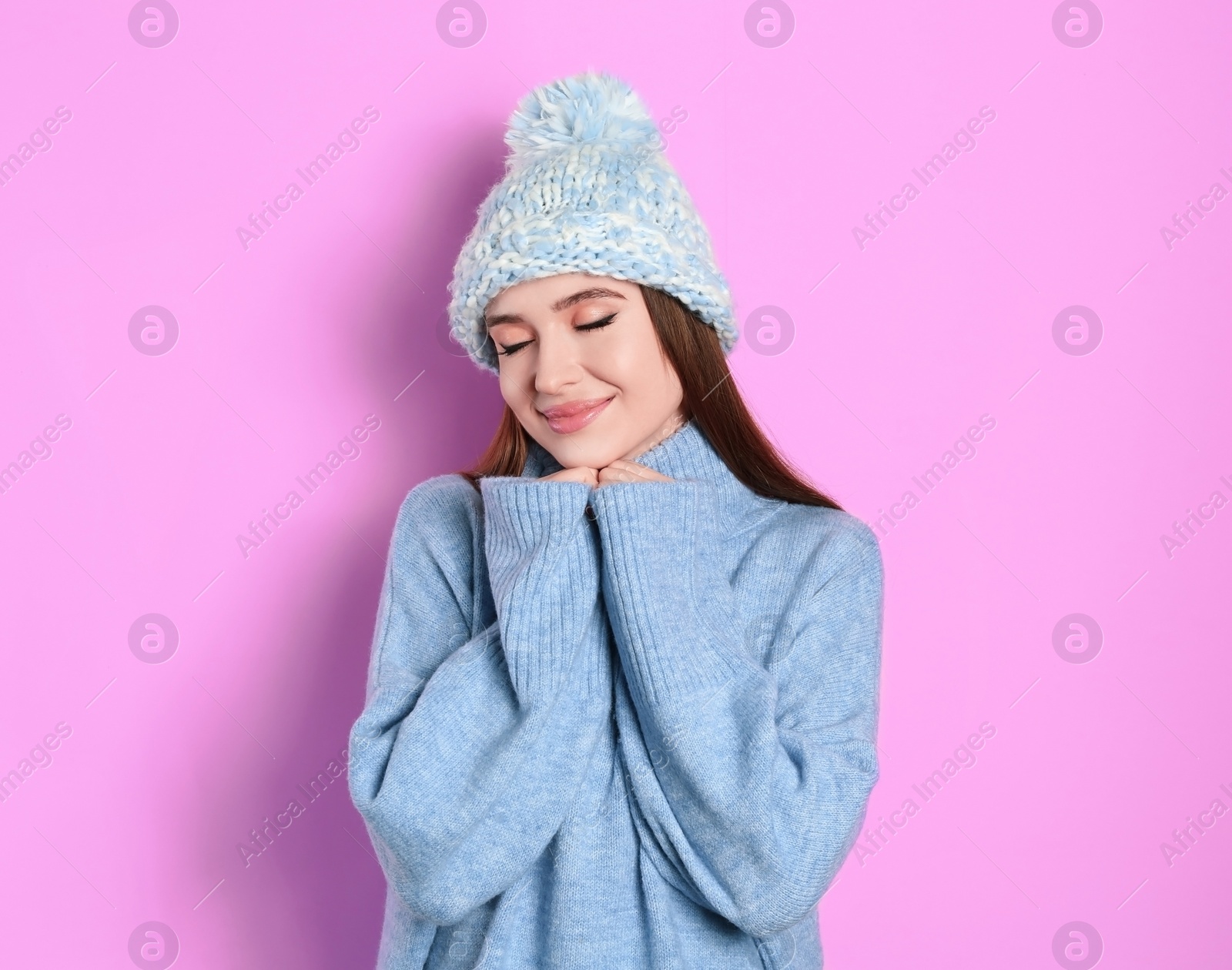 Photo of Young woman wearing warm sweater and hat on pink background. Winter season