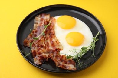 Fried eggs, bacon and microgreens on yellow background