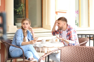 Young couple arguing while sitting in cafe, outdoors. Problems in relationship