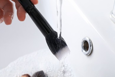 Photo of Woman washing makeup brush under stream of water in sink, closeup