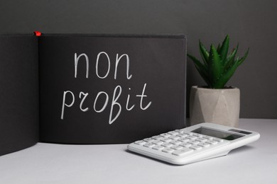 Photo of Black sketchbook with phrase Non Profit, calculator and houseplant on white table
