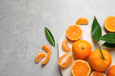 Photo of Fresh ripe tangerines and leaves on grey table, flat lay. Citrus fruit