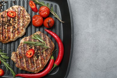 Photo of Grill pan with delicious pork steaks, spices and vegetables on grey table, top view. Space for text