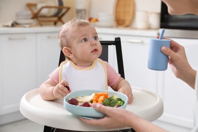 Photo of Mother feeding her cute little baby in kitchen