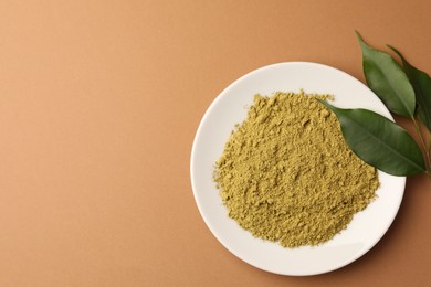 Photo of Henna powder and green leaves on coral background, flat lay with space for text. Natural hair coloring