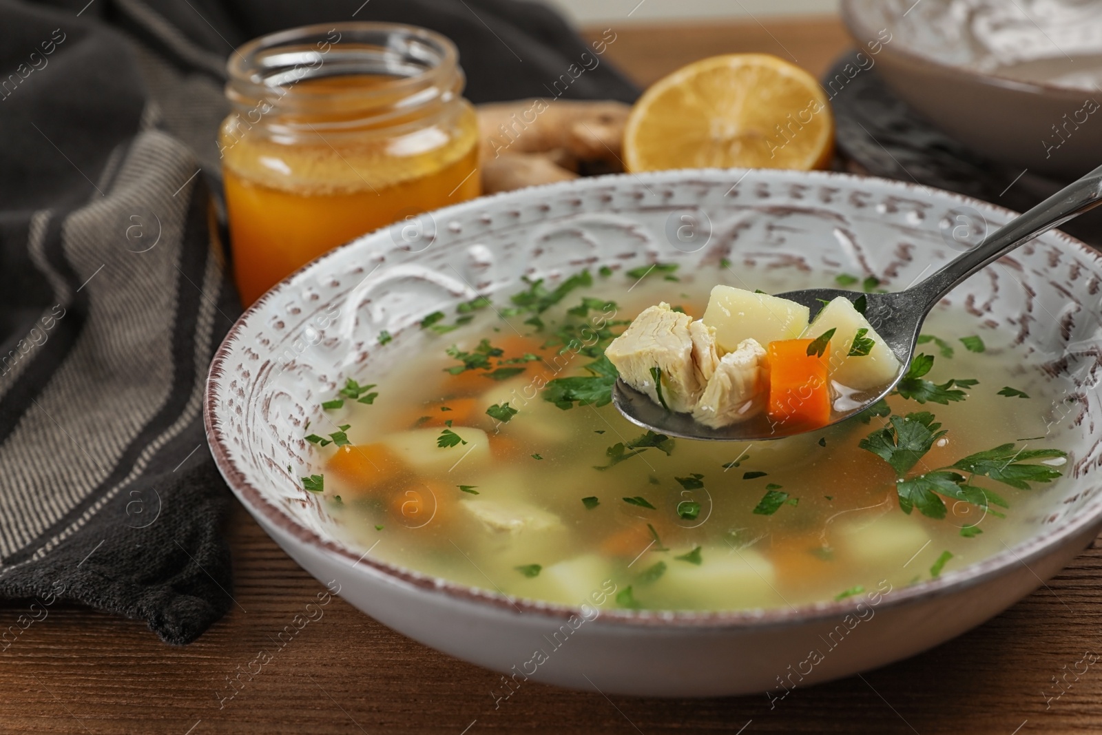 Photo of Spoon with fresh homemade soup to cure flu over bowl on wooden table