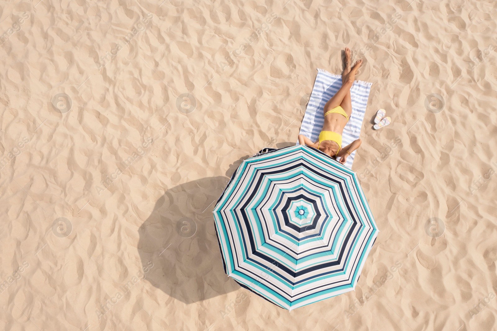 Image of Woman resting under striped beach umbrella at sandy coast, aerial view. Space for text