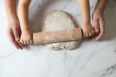 Photo of Father and child rolling raw dough at white table, top view