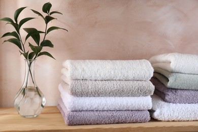 Photo of Stacked soft towels and green leaves on wooden shelf indoors