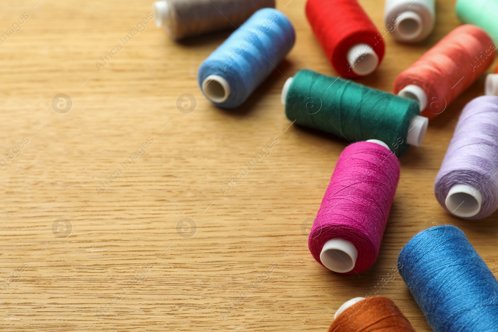 Photo of Many colorful sewing threads on wooden table. Space for text