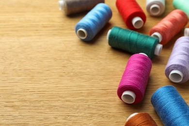 Photo of Many colorful sewing threads on wooden table. Space for text