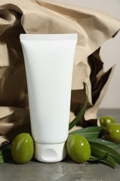 Tube of cream with olive essential oil and kraft crumpled paper on dark grey table, closeup