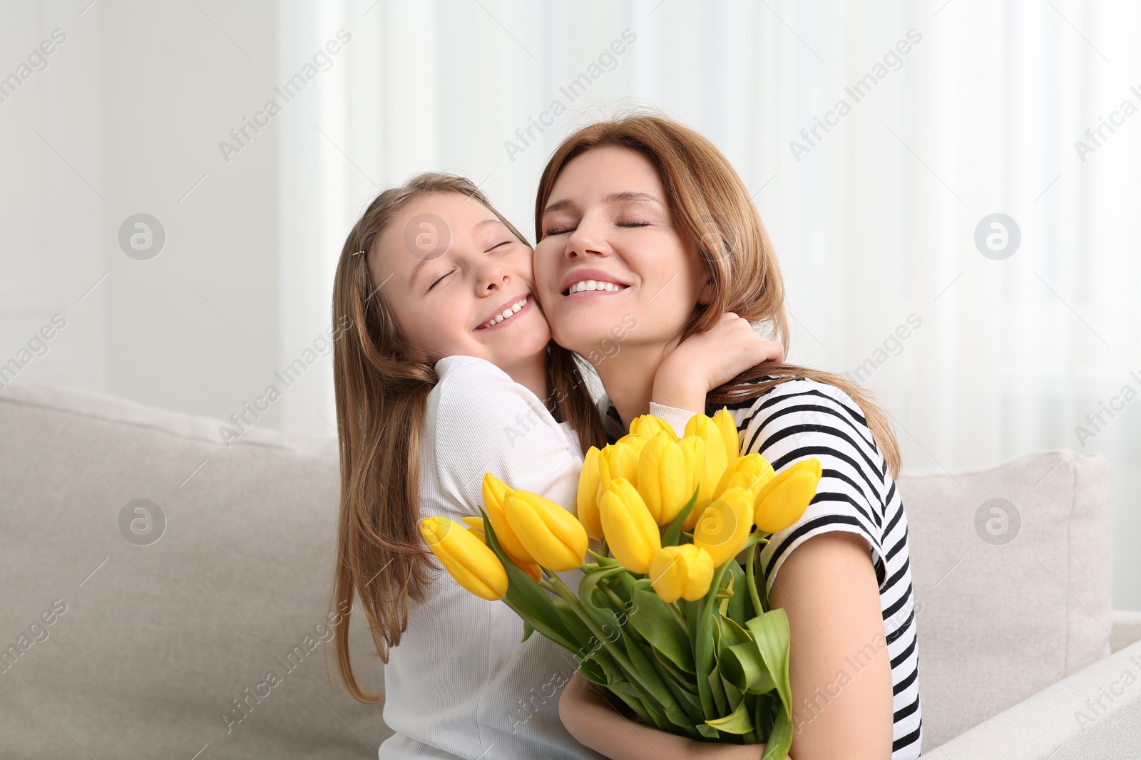 Photo of Happy mother and her cute daughter with bouquet of yellow tulips on sofa at home