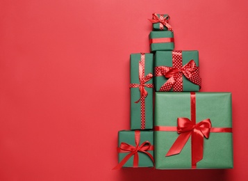 Photo of Christmas tree shape of gift boxes on red background, flat lay. Space for text