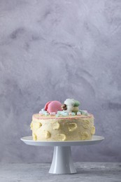 Photo of Delicious cake decorated with macarons and marshmallows on grey table, space for text