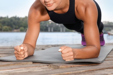 Young woman doing plank exercise on wooden pier near river, closeup