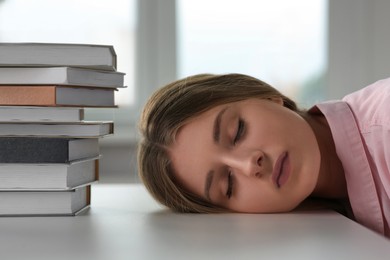 Photo of Young tired woman sleeping near books at white table indoors, closeup