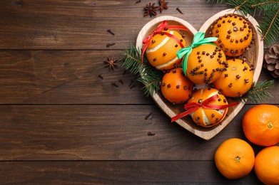 Pomander balls made of tangerines with cloves and fir branches on wooden table, flat lay. Space for text