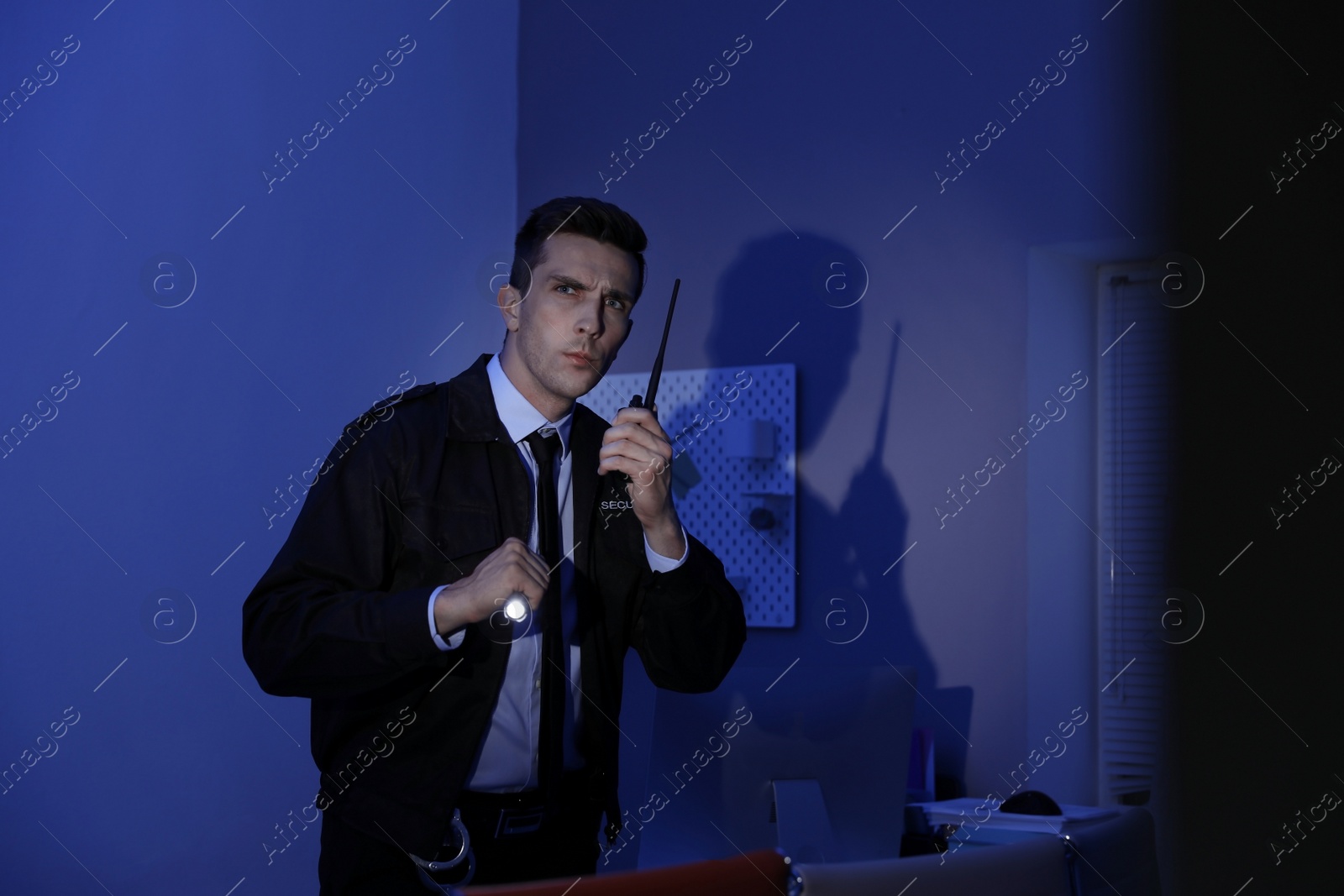 Photo of Male security guard with flashlight and portable radio transmitter in dark room