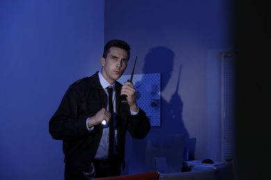 Male security guard with flashlight and portable radio transmitter in dark room