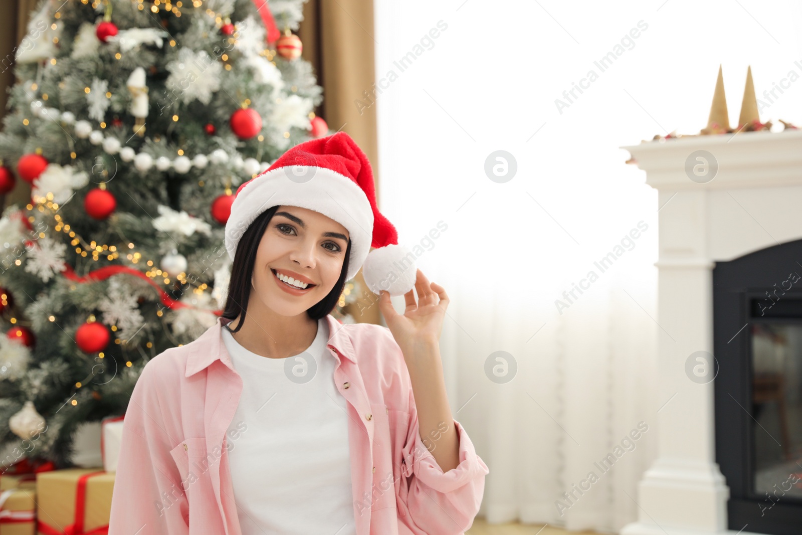 Photo of Young woman in Santa hat near Christmas tree at home