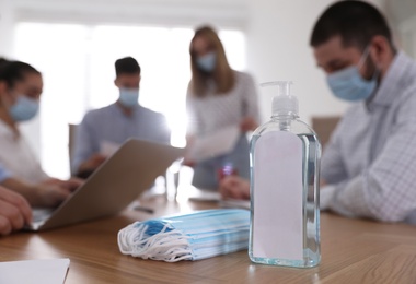 Protective masks, hand sanitizer and blurred view of coworkers on background. Business meeting during COVID-19 pandemic