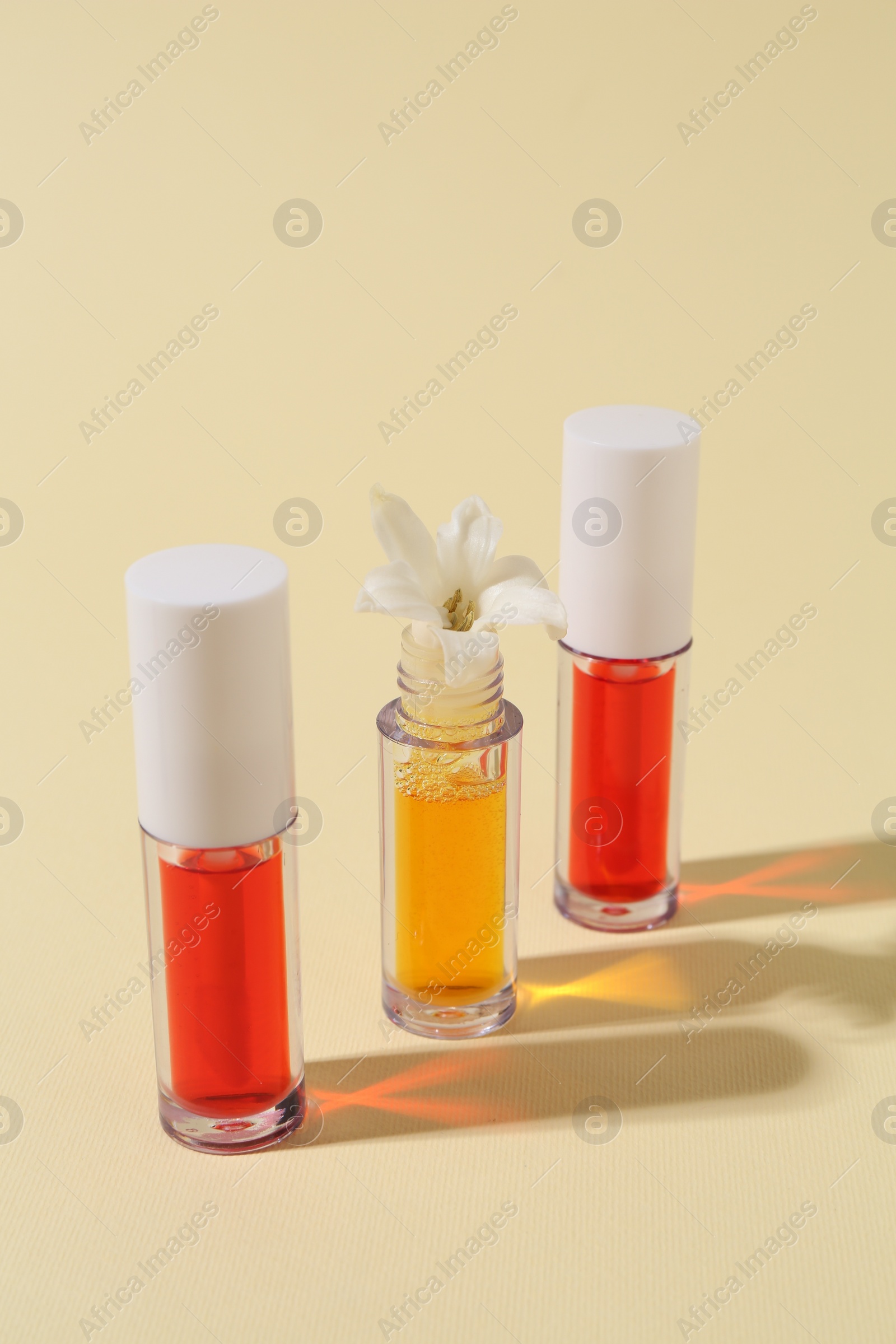 Photo of Bright lip glosses and flower on beige background