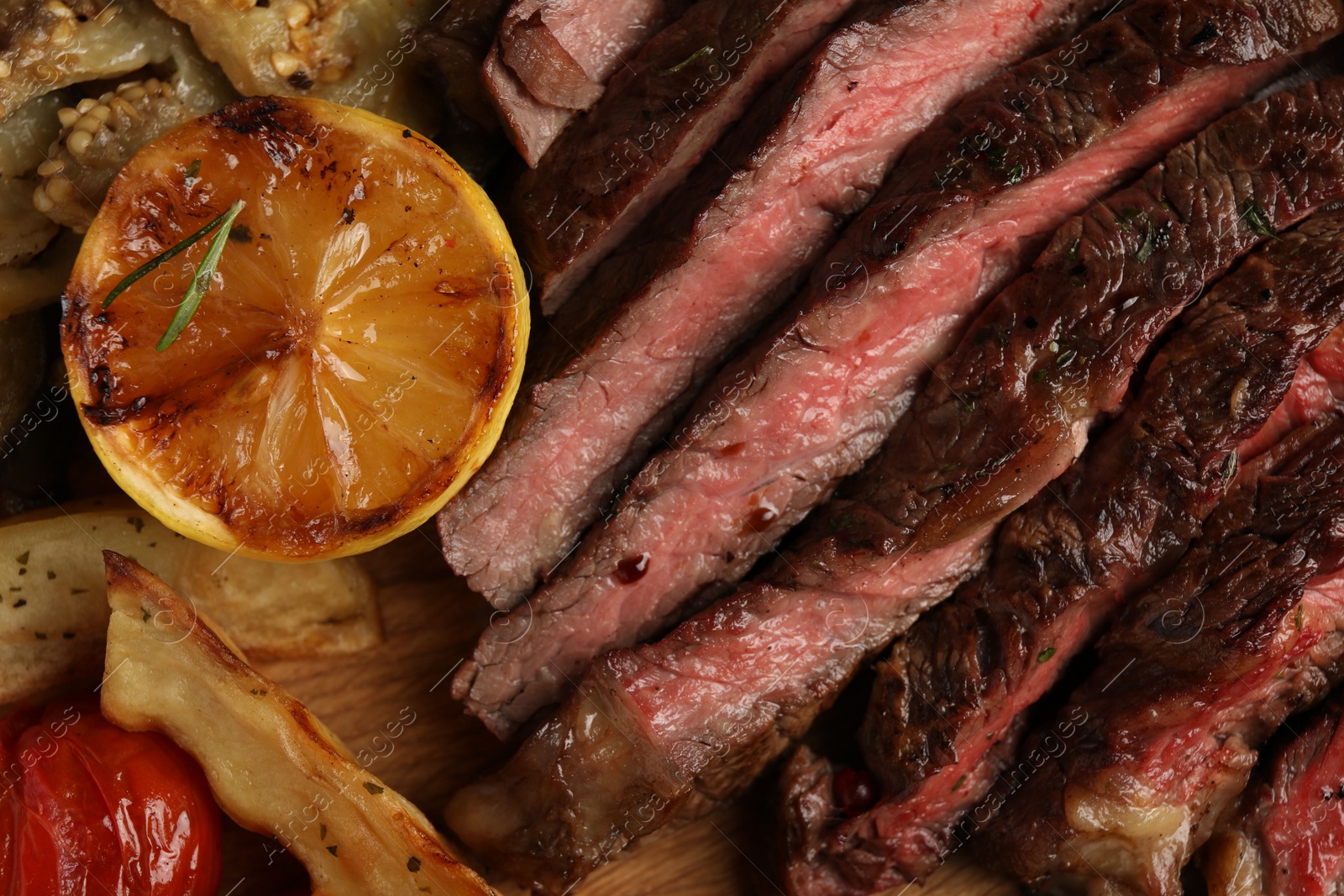 Photo of Delicious grilled beef with vegetables, lemon and spices on table, top view