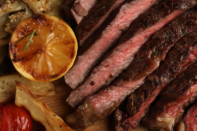 Photo of Delicious grilled beef with vegetables, lemon and spices on table, top view