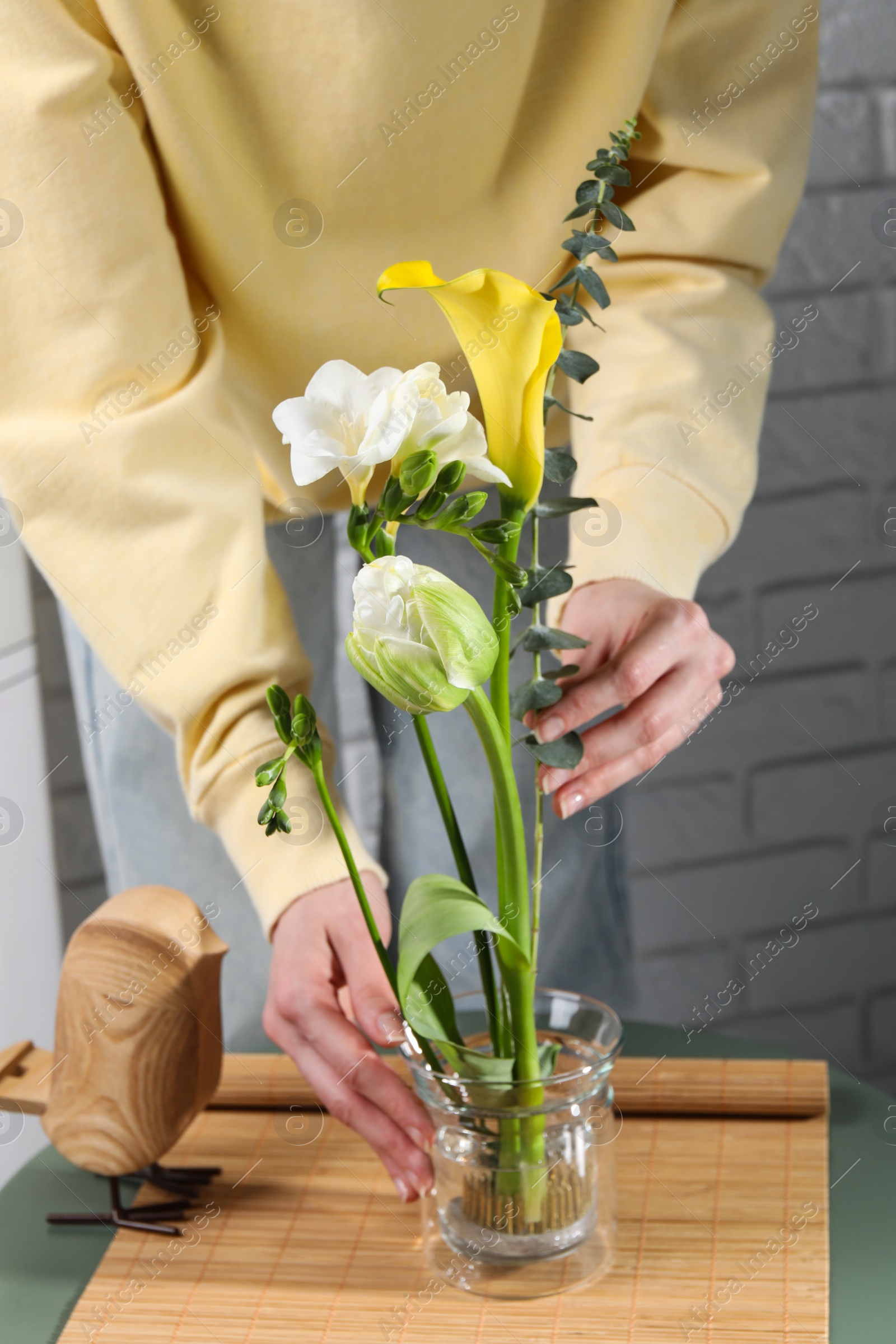 Photo of Beautiful ikebana for stylish house decor. Woman create floral composition with fresh flowers and eucalyptus branch at coffee table, closeup