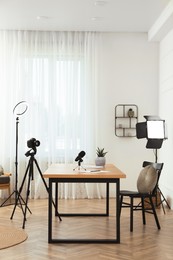 Camera and lighting equipment on tripods near table in room. Blogger workplace