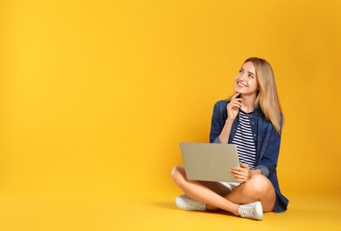 Photo of Happy young woman with laptop on yellow background. Space for text