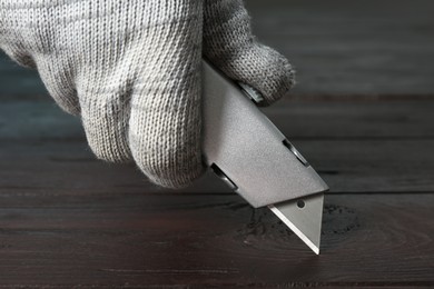 Photo of Man using utility knife at wooden table, closeup