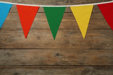 Bunting with colorful triangular flags on wooden background, space for text