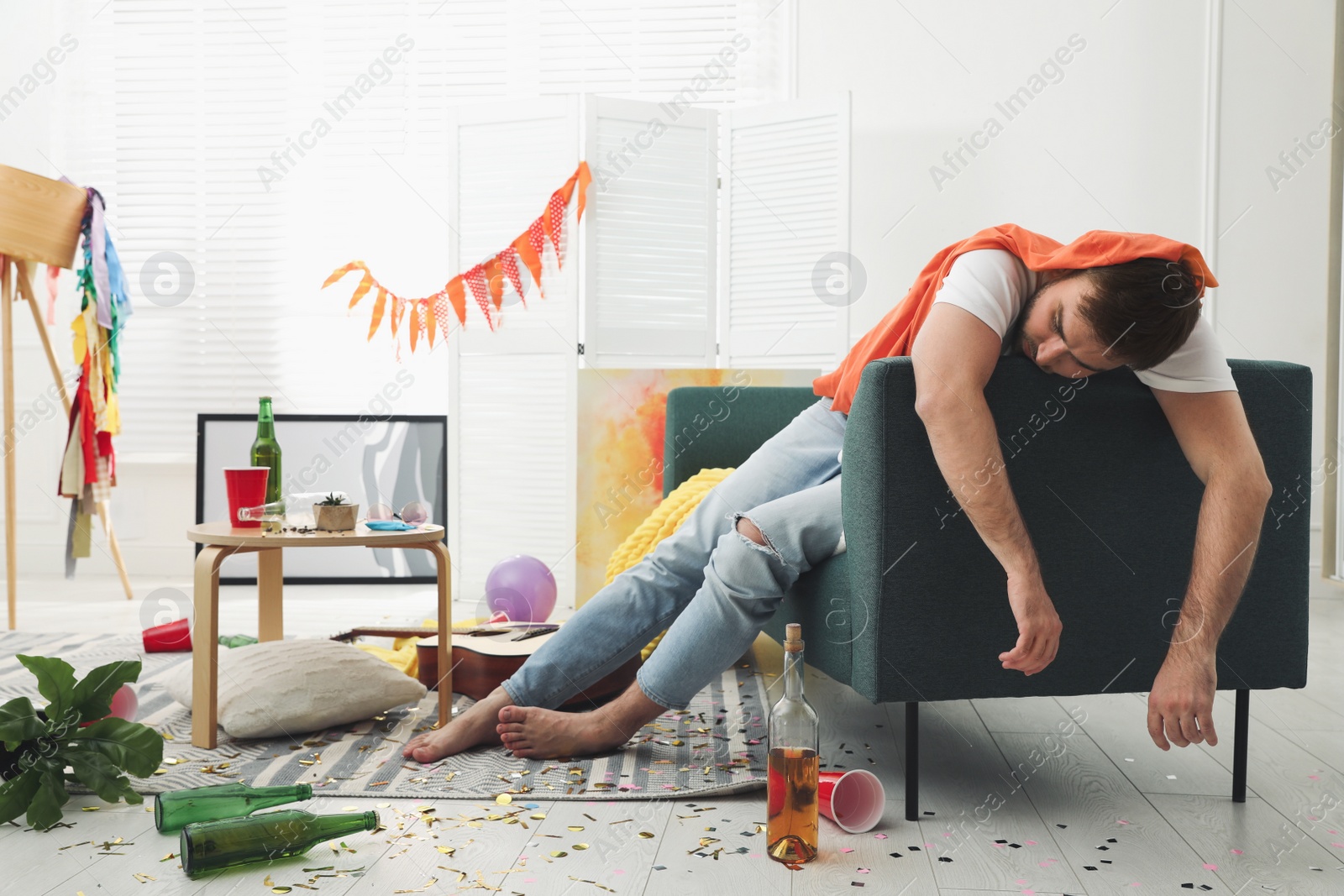 Photo of Young man sleeping on sofa in messy room after party