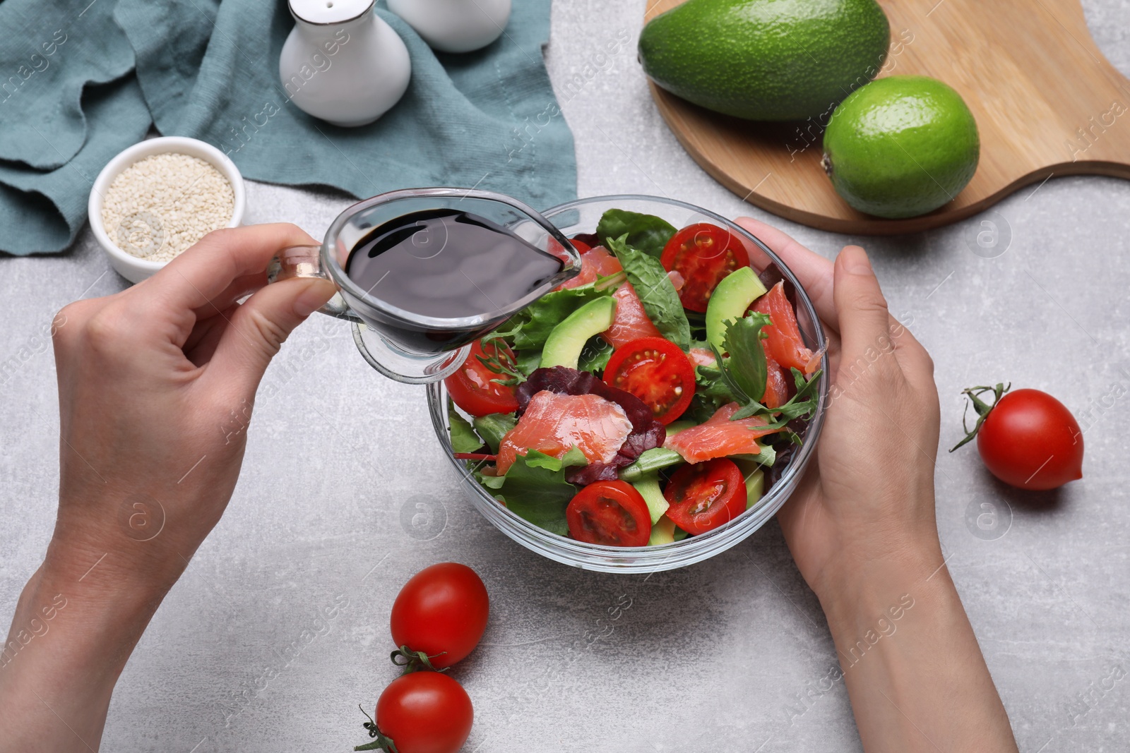 Photo of Woman adding soy sauce to tasty salad at grey table, closeup