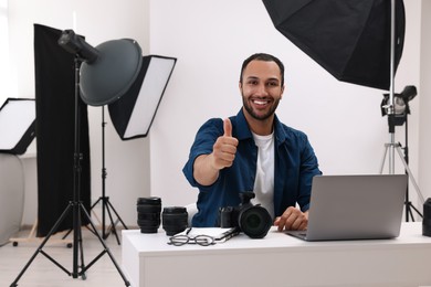 Photo of Young professional photographer with camera showing thumbs up in modern photo studio