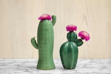 Photo of Trendy cactus shaped ceramic vases with flowers on table against wooden background