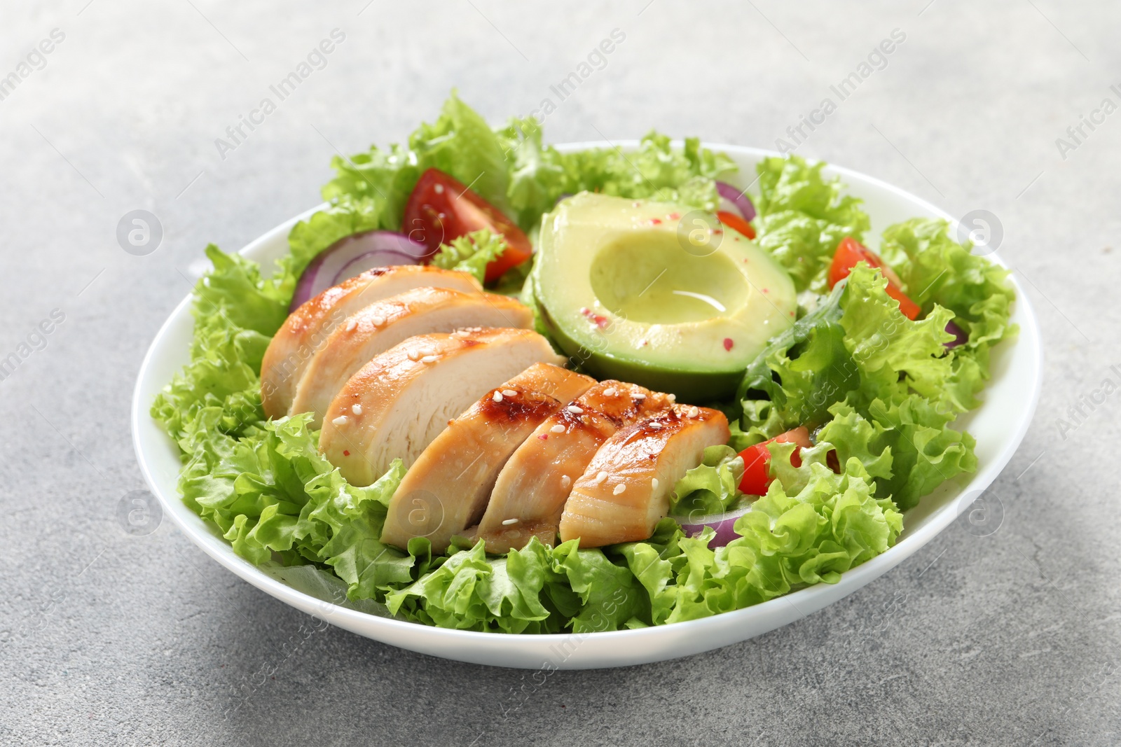 Photo of Delicious salad with chicken, avocado and vegetables on light grey table, closeup