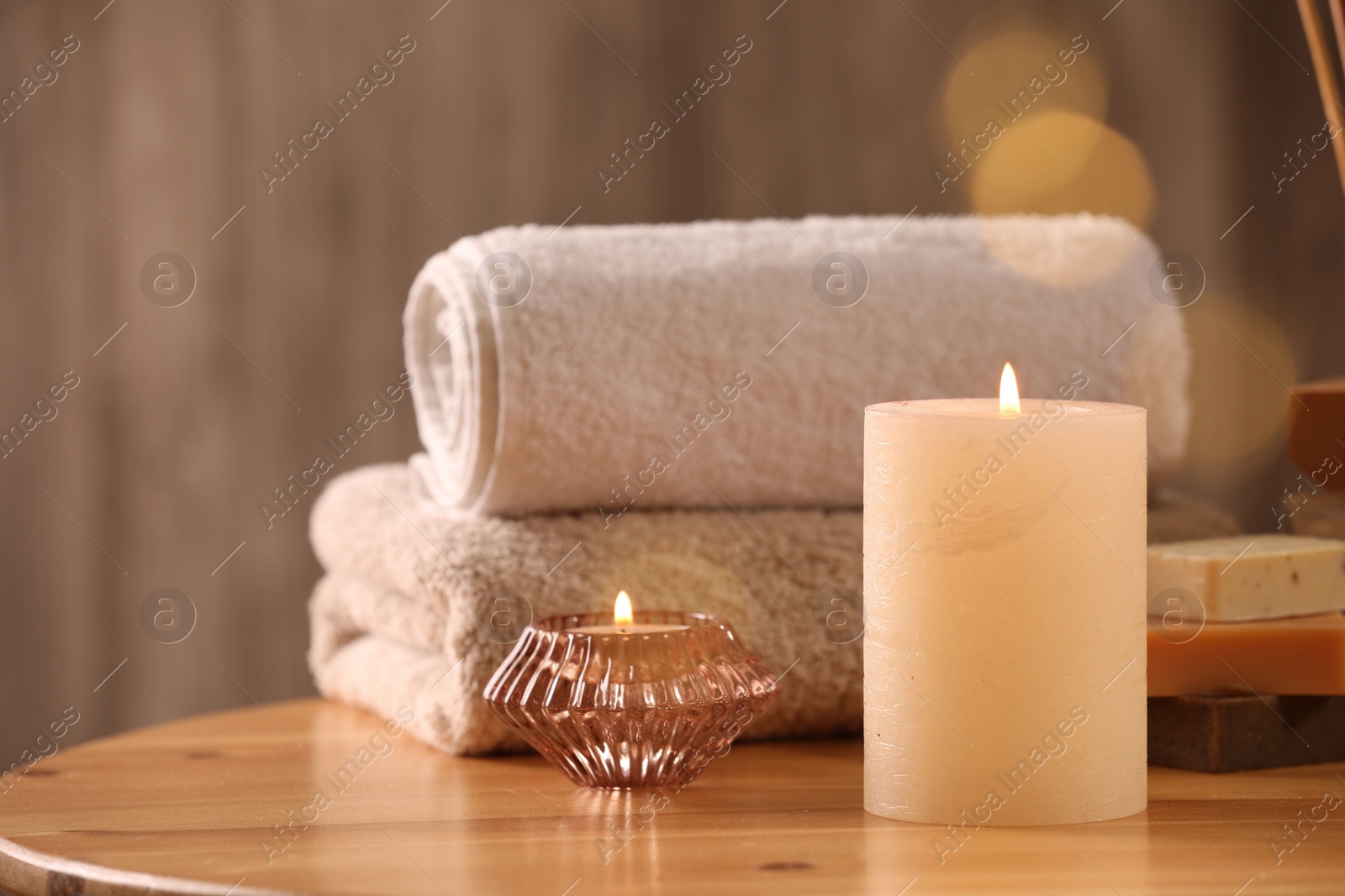 Photo of Spa composition. Burning candles, towels and soap on wooden table, space for text