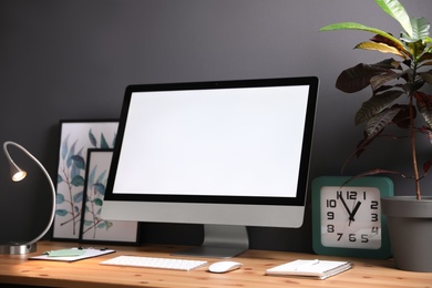 Comfortable workplace with modern computer on wooden table near black wall. Space for text