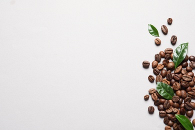 Fresh green coffee leaves and beans on light background, flat lay. Space for text