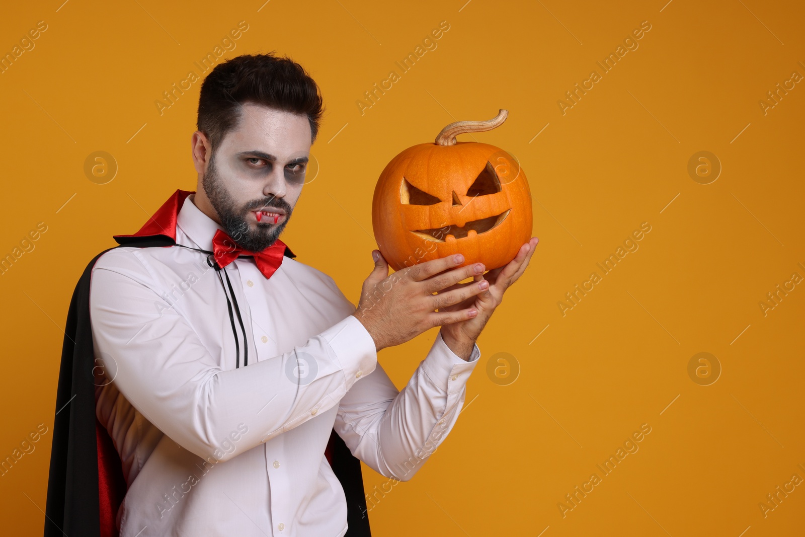 Photo of Man in scary vampire costume with fangs and carved pumpkin on orange background, space for text. Halloween celebration