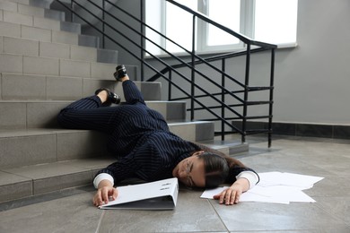 Photo of Unconscious woman with scattered folder and papers lying on floor after falling down stairs indoors