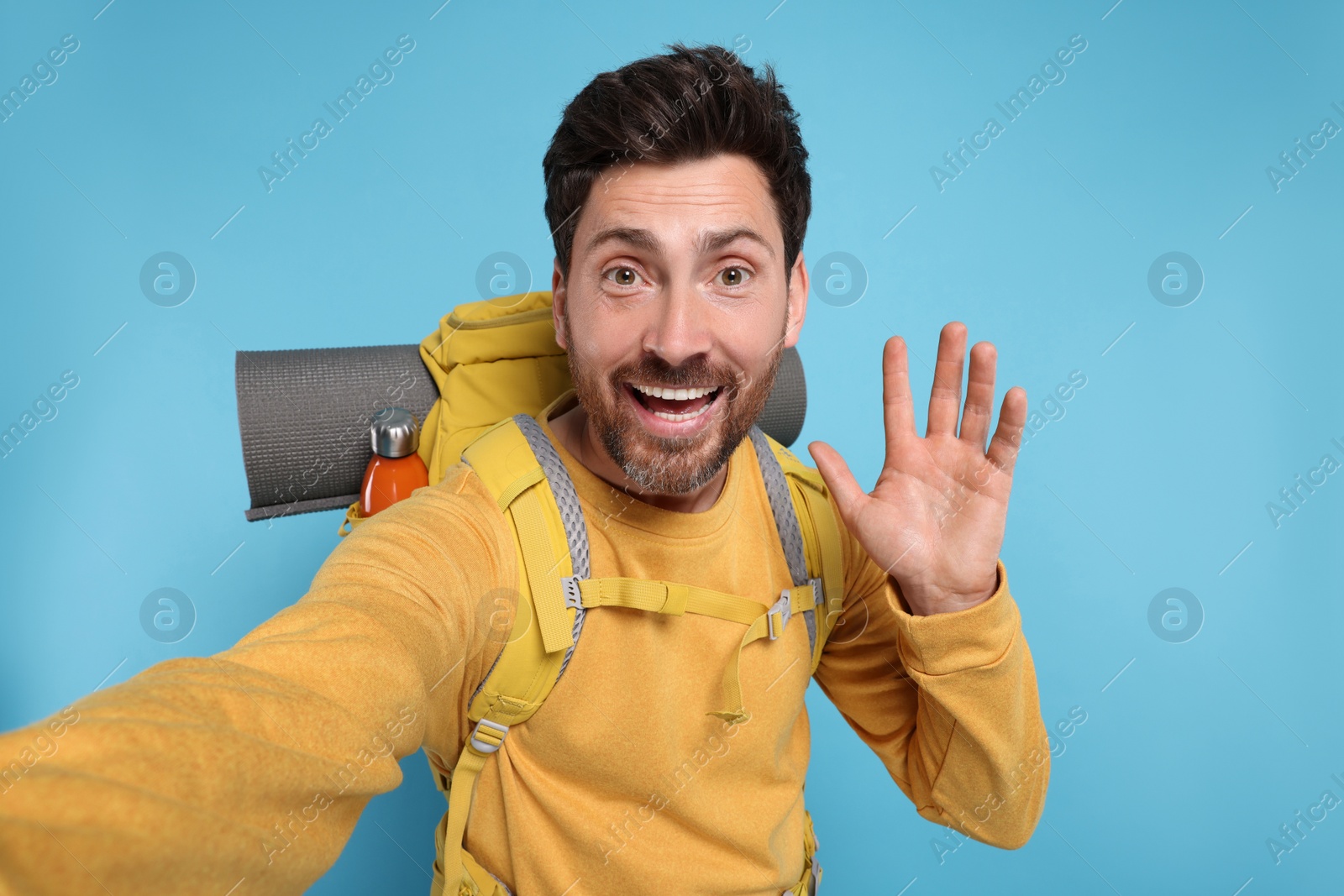 Photo of Happy man with backpack taking selfie on light blue background. Active tourism