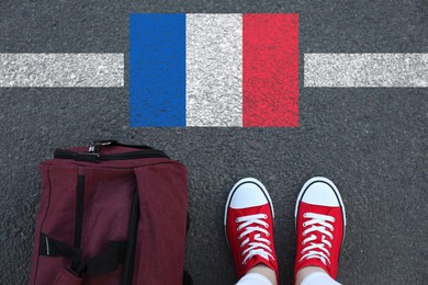 Image of Immigration. Woman with bag standing on asphalt near flag of France, top view