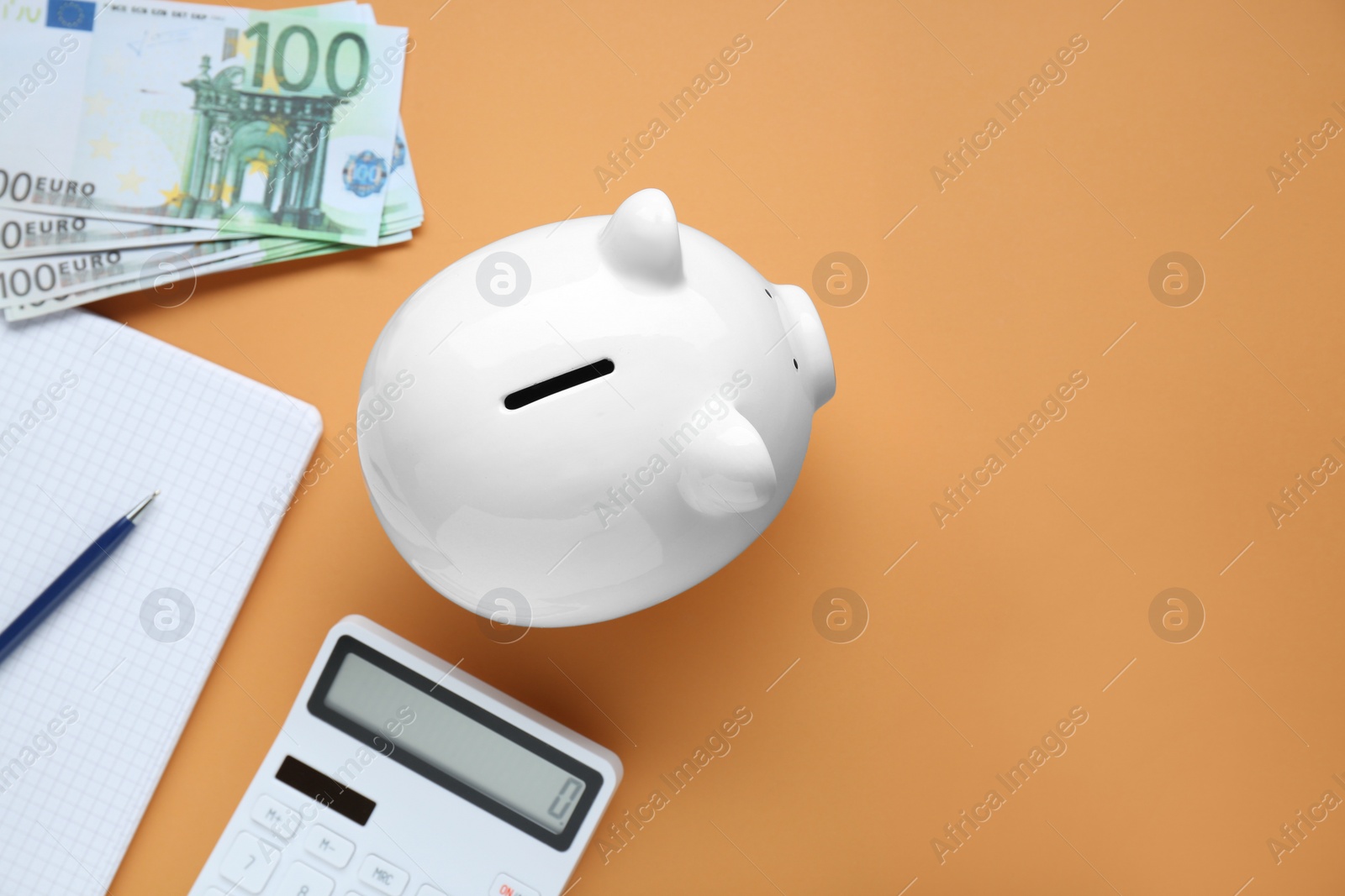 Photo of Piggy bank, banknotes, calculator and notebook on orange background, flat lay. Space for text