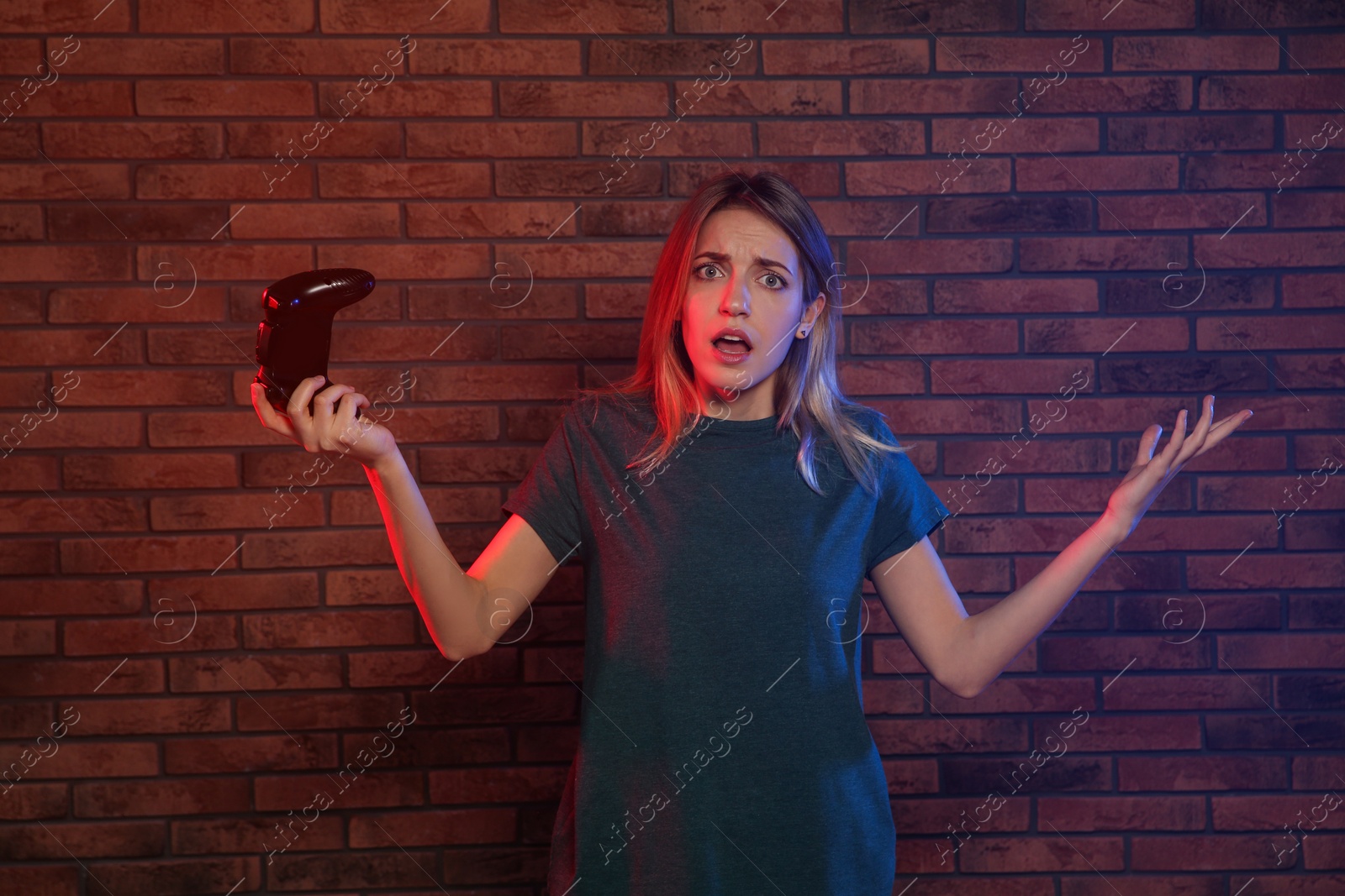 Photo of Emotional young woman playing video games with controller near brick wall