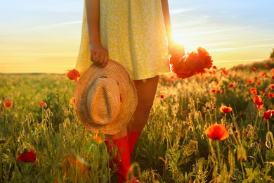 Photo of Woman with straw hat and bouquet of poppies in sunlit field, closeup