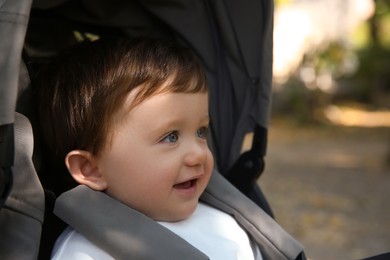 Cute little child in baby stroller outdoors, space for text